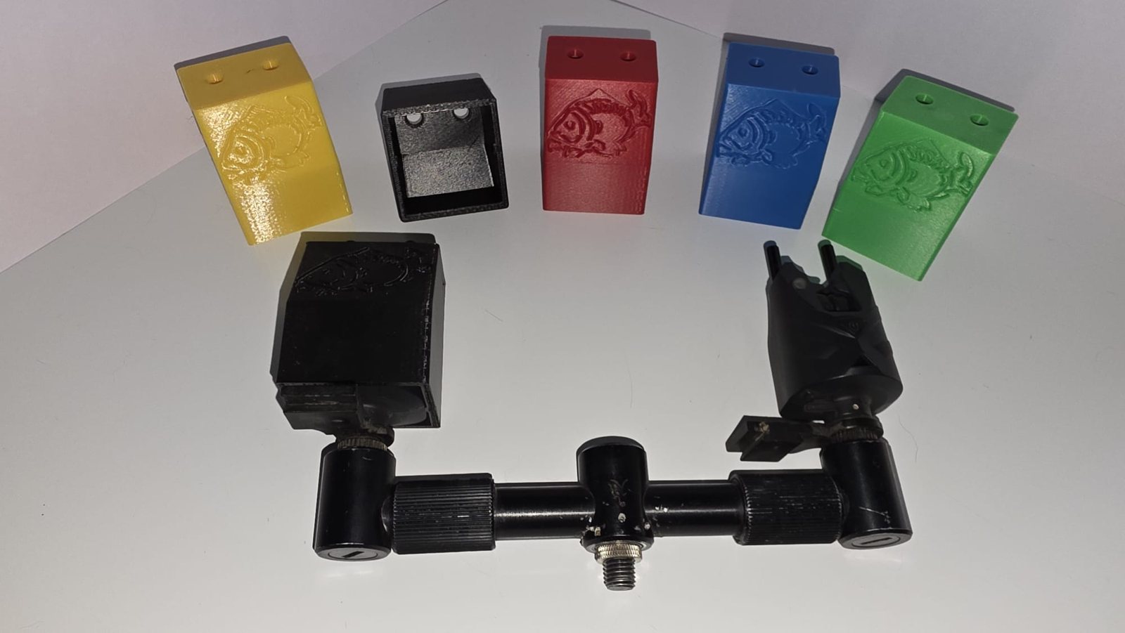 Five 3D printed ND S9 bite alarm protection covers in yellow, black, red, blue and green, each embossed with a carp design, shown alongside bite alarms on a buzz bar